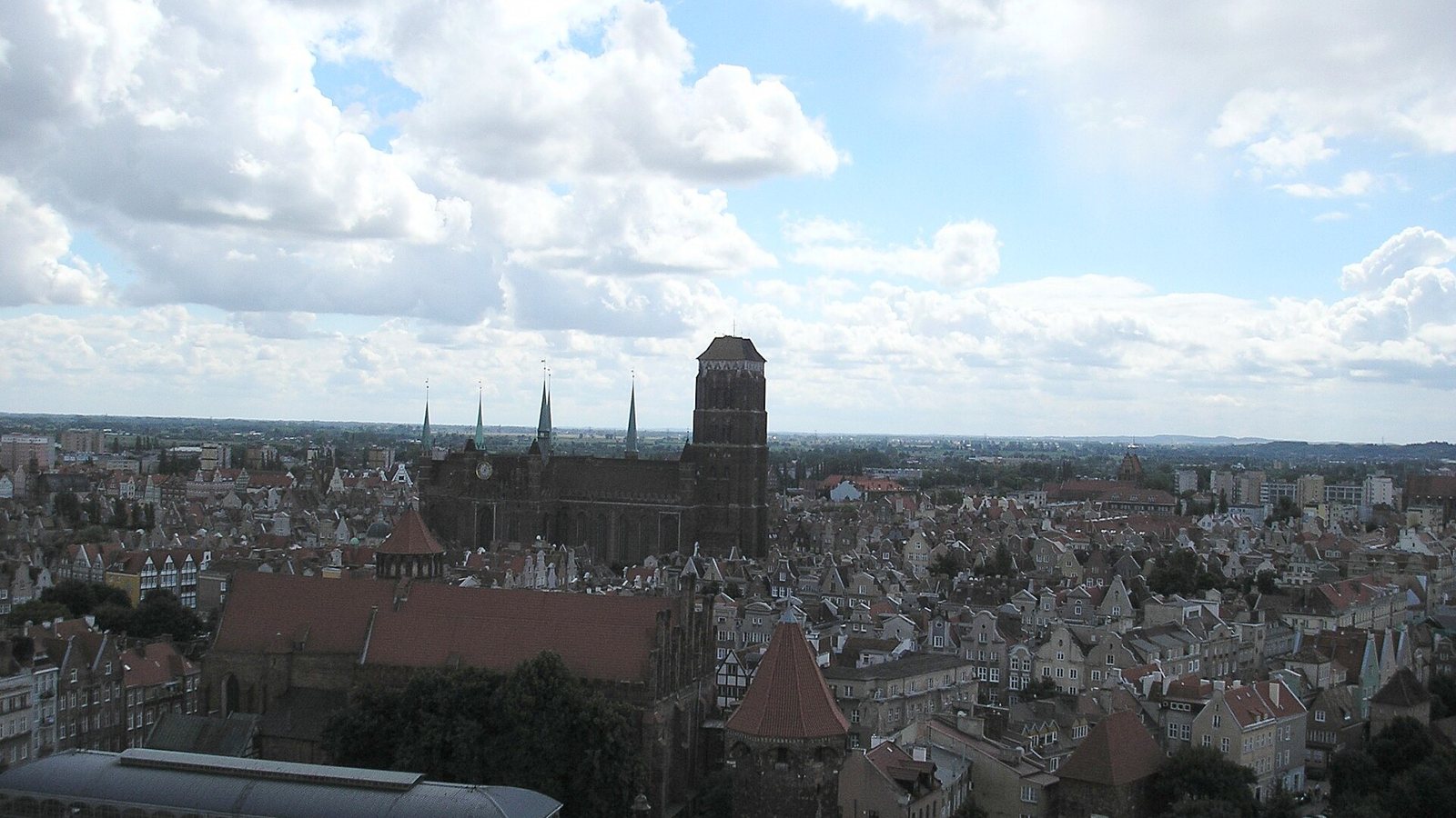 Aerial panorama of Gdańsk Main Town with St. Mary's Basilica and red-roofed townhouses, seen from a tower.